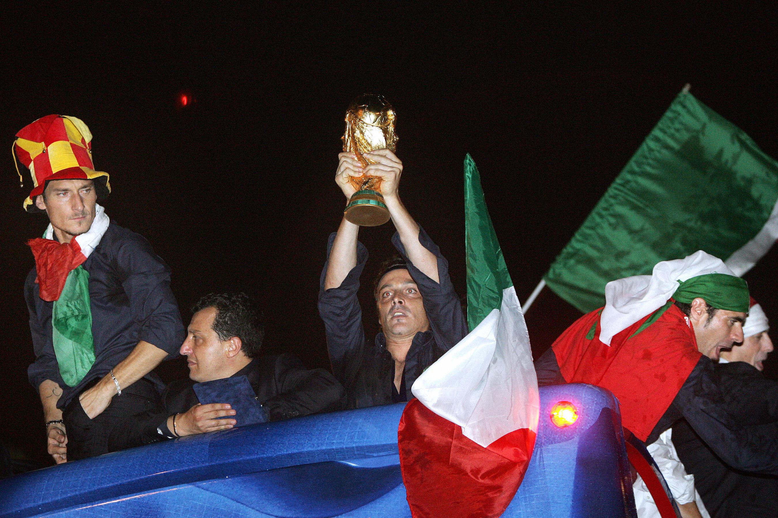 Rome, ITALY:  Italian football player Francesco Totti (L), wearing the AS Roma hat, looks at the World Cup trophy held by teammate Massimo Oddo as the Italian team celebrated their victory with fans Circo Massimo in Rome 10 July 2006. Italy\\'s jubilant World Cup winners arrived back home with the coveted trophy Monday amid a welter of excitement in Rome as fans gave them an emotional reception on the streets of the capital. AFP PHOTO  ANDREAS SOLARO  (Photo credit should read ANDREAS SOLARO/AFP/Getty Images)